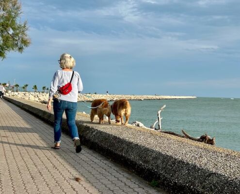 Frau wandert mit Hunden an der Promenade von Caorle in Italien entlang